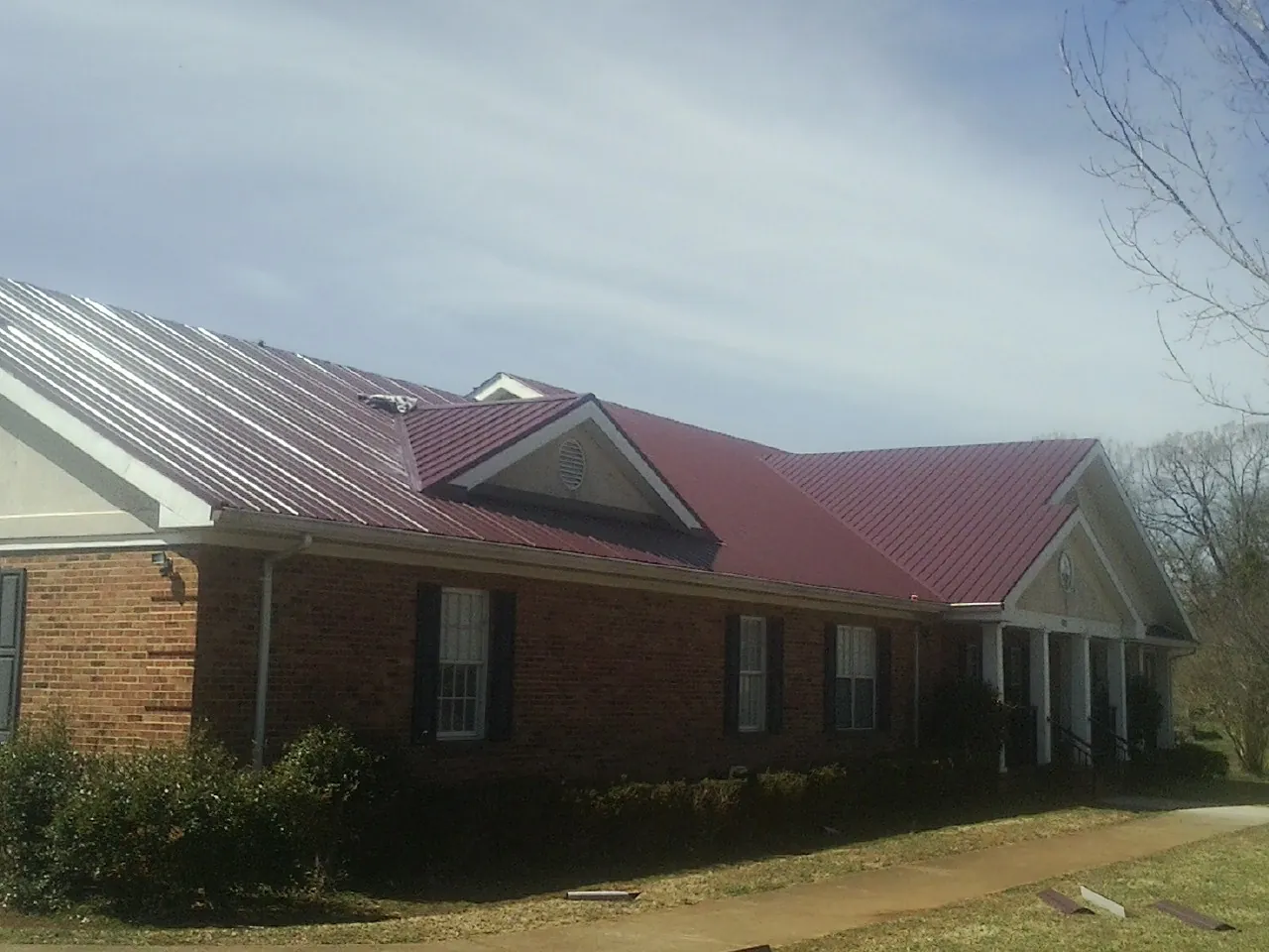 Red metal roof with gabled entries on a long brick building, from a Hail Damage Roof Repair job in Sherman