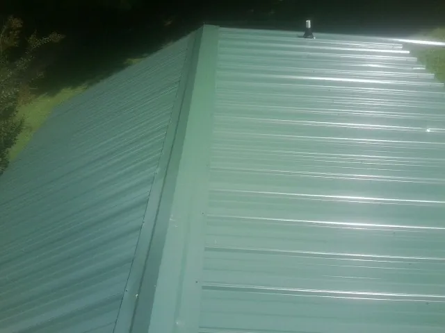 New green metal panels meeting at the ridge of a roof — Flat Roof Repair work by our crew in Sherman